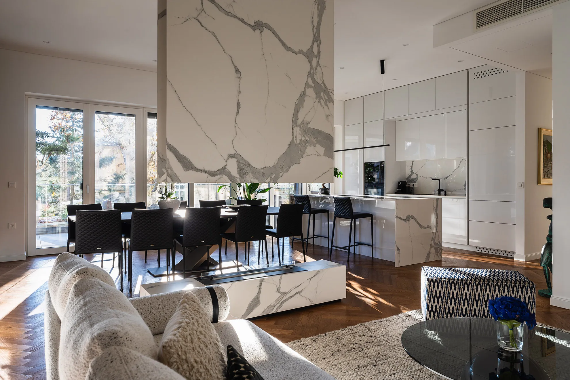 Open-plan living space in Penthouse Schellenburg with large windows, designer furniture, and marble accents, combining style and comfort in a minimalist yet luxurious setting.