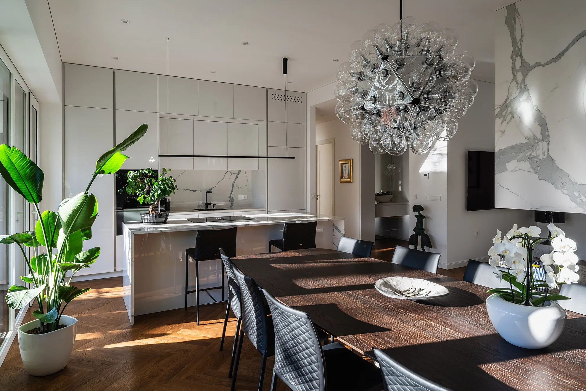 Contemporary dining area in Penthouse Schellenburg with a statement chandelier, sleek furniture, and large windows, creating an airy, light-filled space for meals and gatherings.