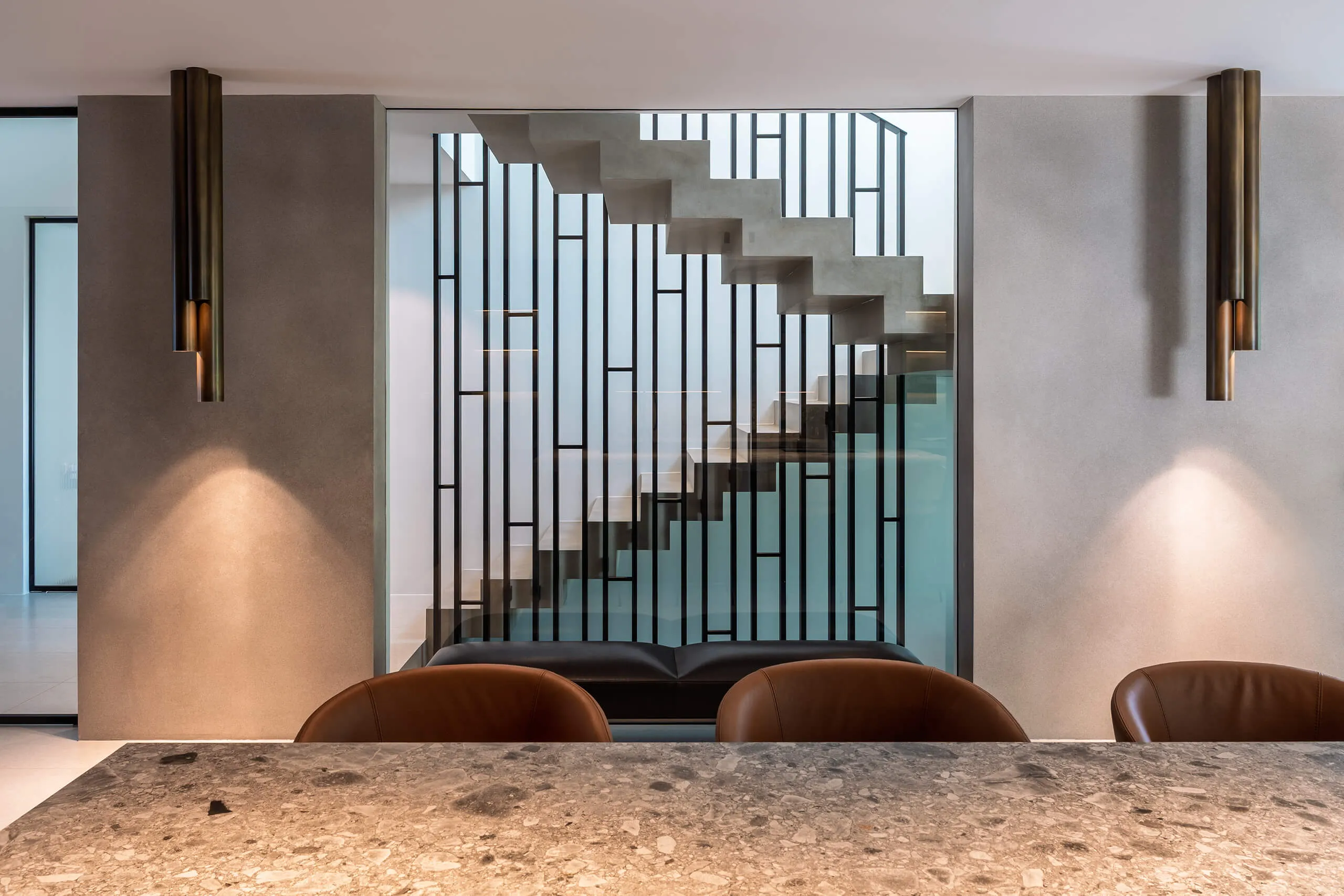 Sophisticated dining and kitchen space in a contemporary chalet interior by Studio Mosh, featuring pendant lighting, velvet dining chairs, a marble breakfast bar, and a floor-to-ceiling wine display — refined alpine living at its best.