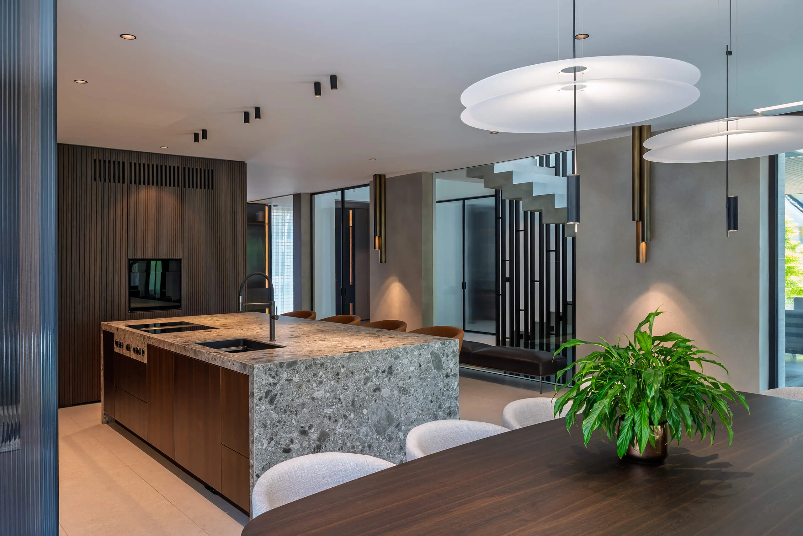 Sophisticated dining and kitchen space in a contemporary chalet interior by Studio Mosh, featuring pendant lighting, velvet dining chairs, a marble breakfast bar, and a floor-to-ceiling wine display — refined alpine living at its best.