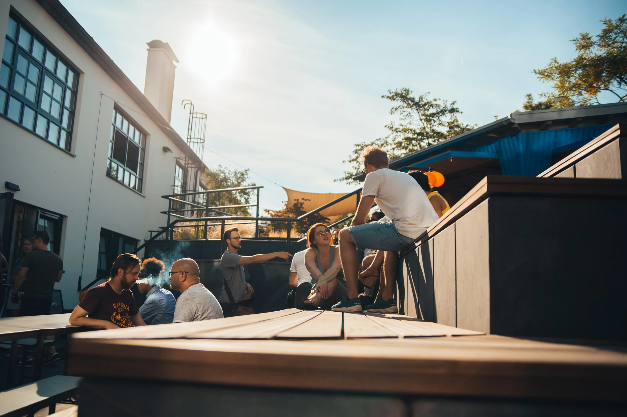 Group of people socializing outdoors on a sunny day near modern buildings and seating area.