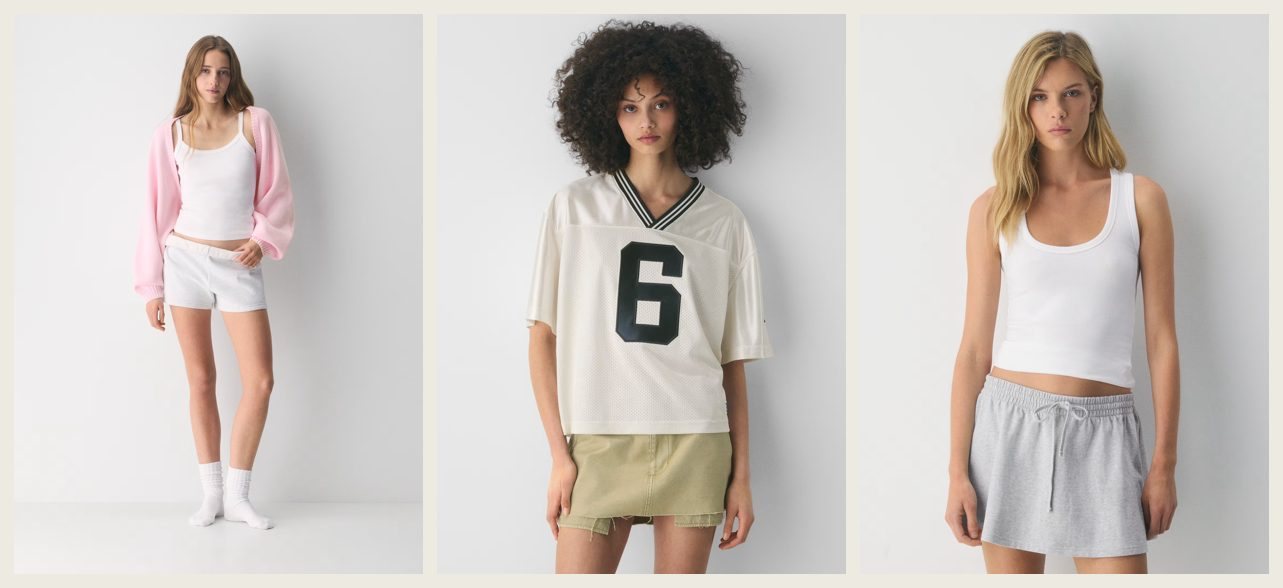 Three product photographs from Aritzia's TNA label. A model in a pink zip hoodie over a white tank top and white shorts; a model with curly hair in a cream mesh football-style jersey with a large black number 6 and a khaki mini skirt; and a model in a white tank top with grey drawstring shorts. The label's tagline reads "You're up for anything. So are your clothes."