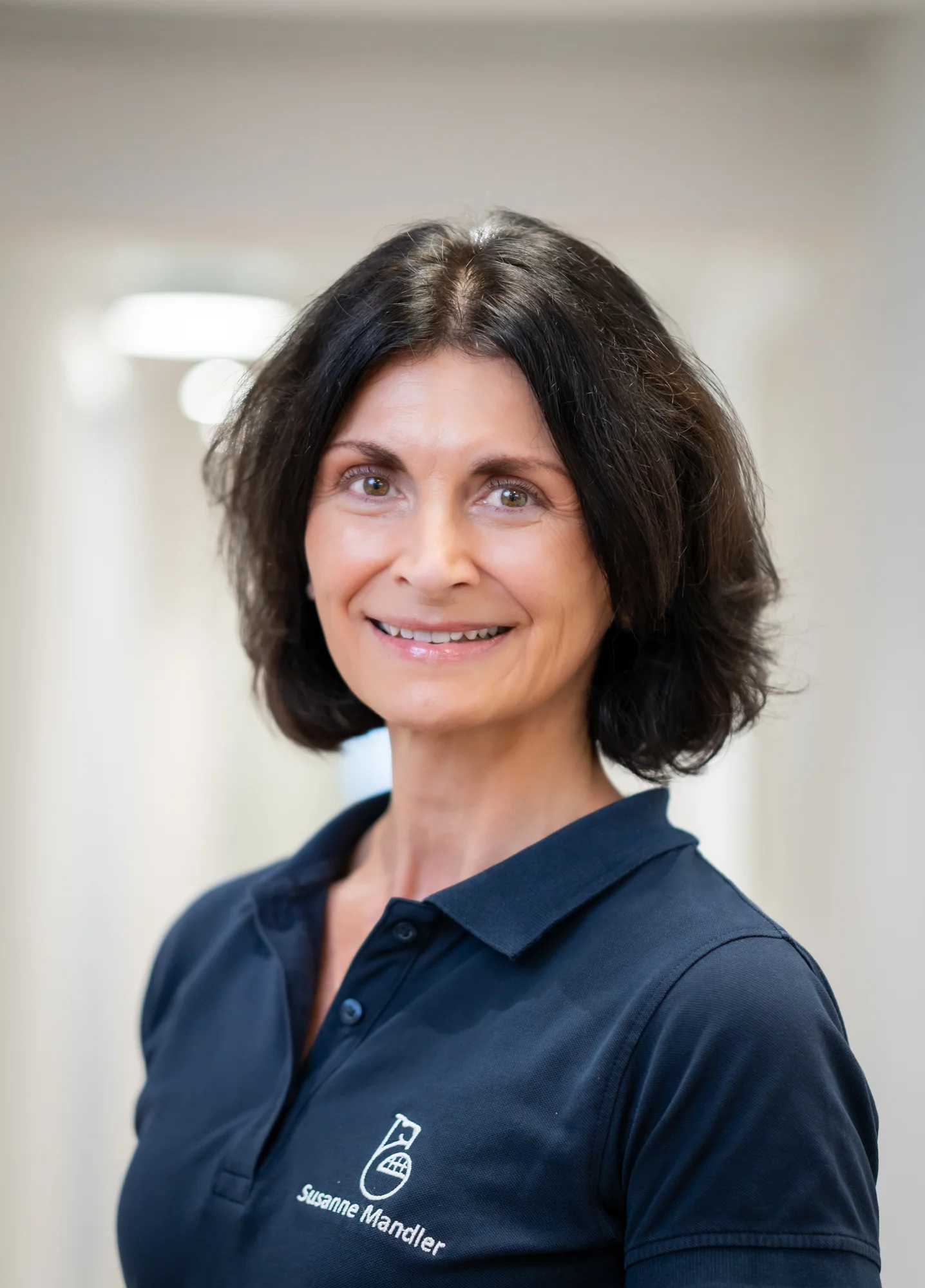 Porträt einer lächelnden Frau mit kurzen dunklen Haaren in einem dunkelblauen Polohemd mit der Aufschrift Susanne Mandler.