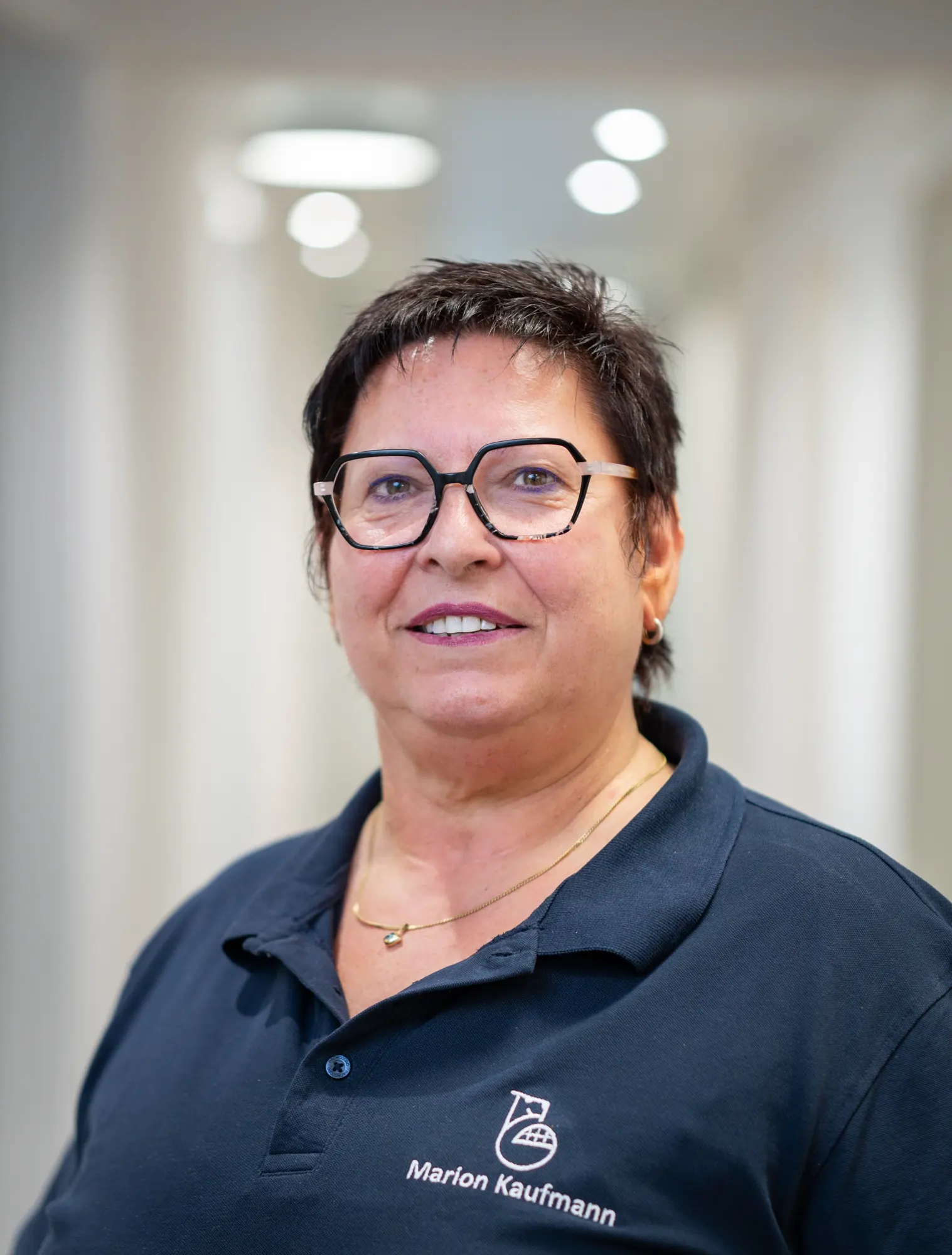 Porträt einer Frau mit kurzen dunklen Haaren, Brille und blauem Poloshirt mit dem Namen Marion Kaufmann.