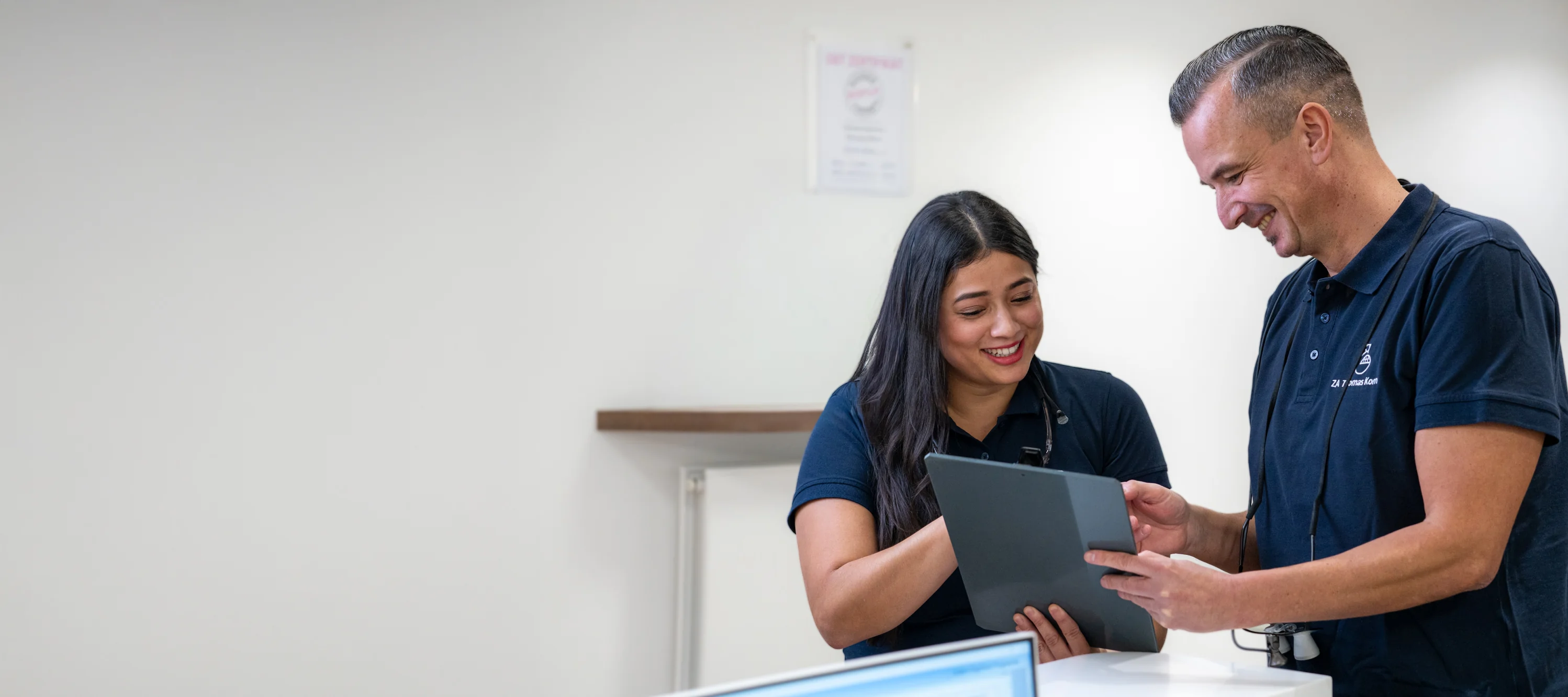Zwei Zahnärzte, ein Mann und eine Frau, lächeln und sehen sich gemeinsam einen Tablet-Bildschirm an.