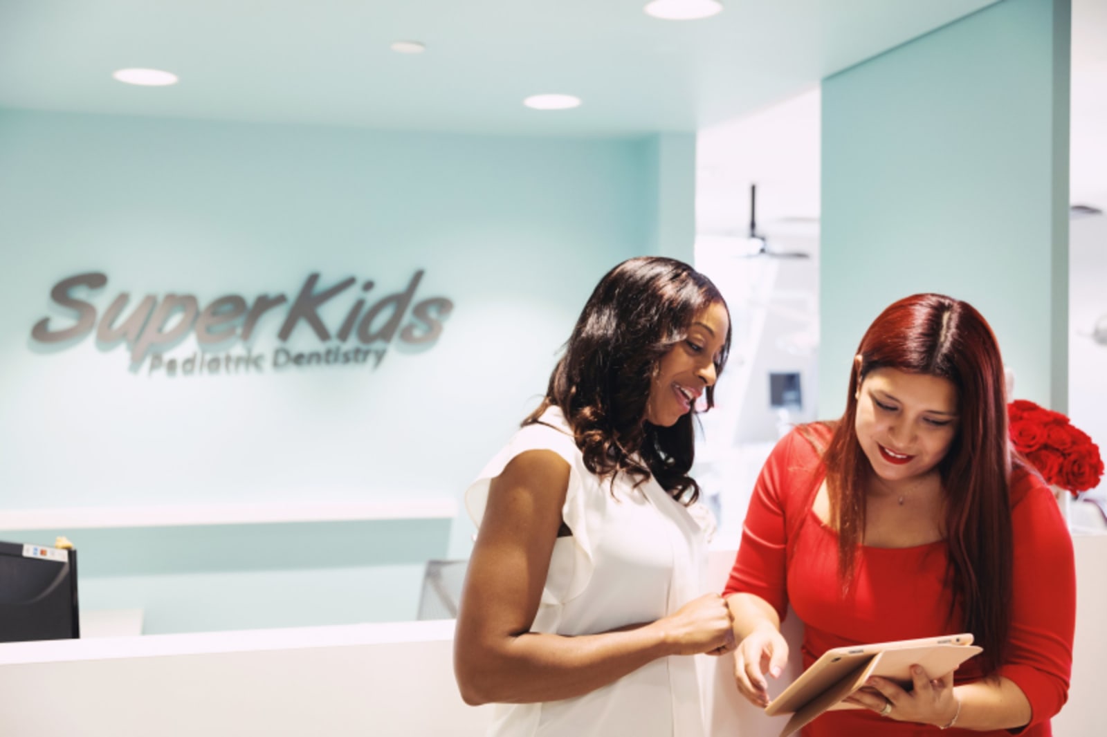 Two young girls smiling at SuperKids dental office location with modern turquoise wall signage