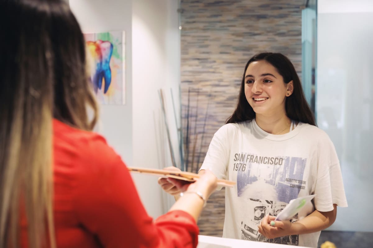 Pediatric dentist discussing orthodontic treatment options with teenage patient in clinical office setting.