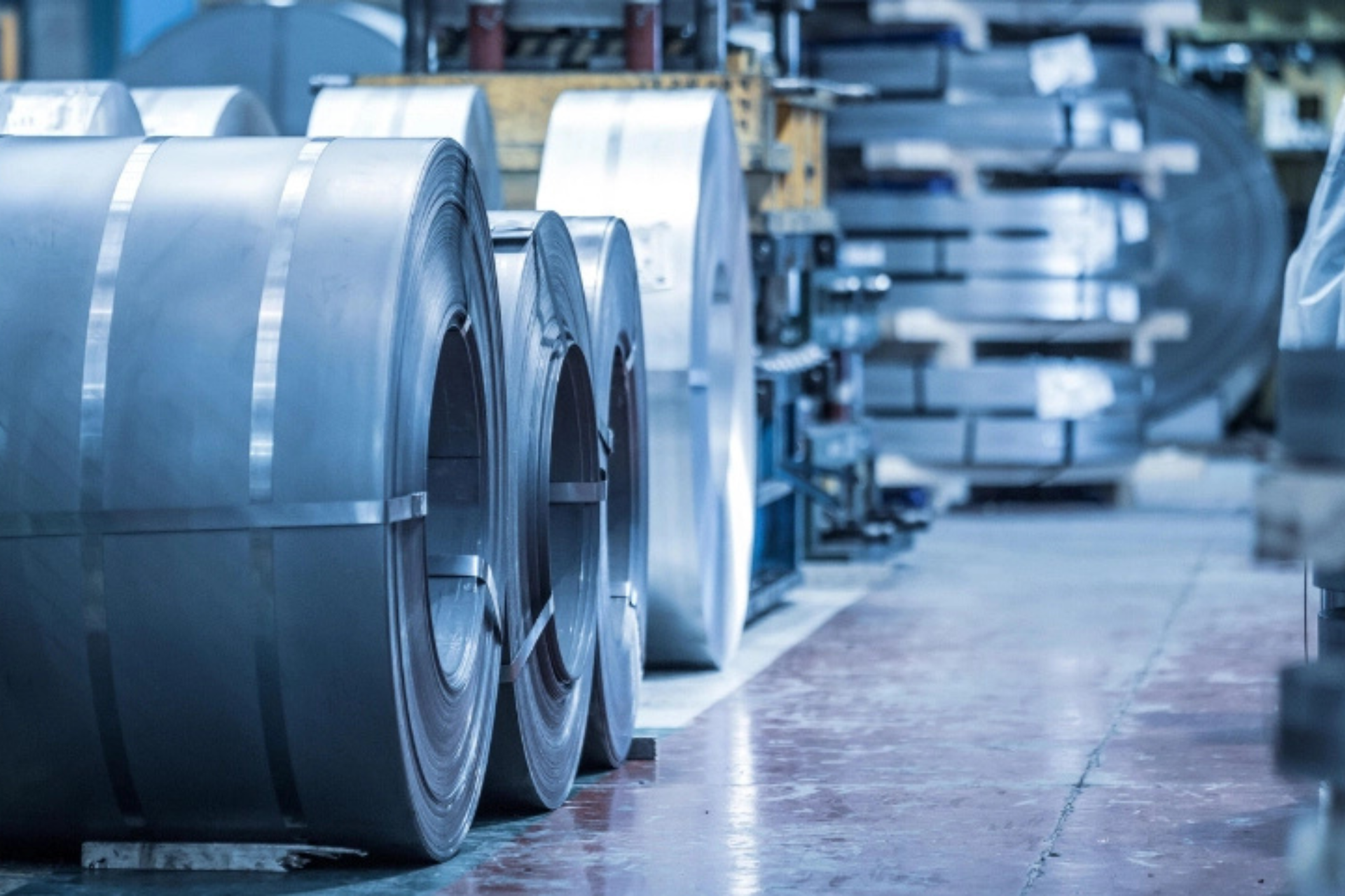 Rolls of coiled sheet steel lined up on the floor of an industrial warehouse