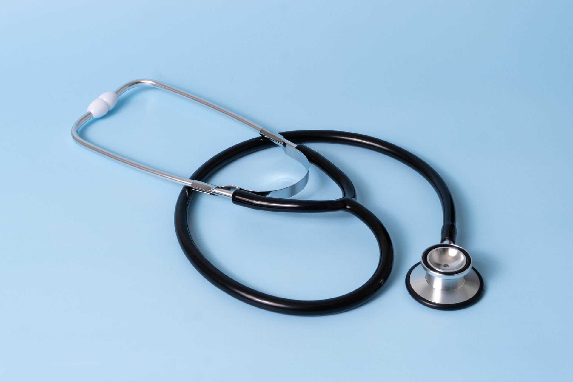 A black stethoscope lying on a light blue background