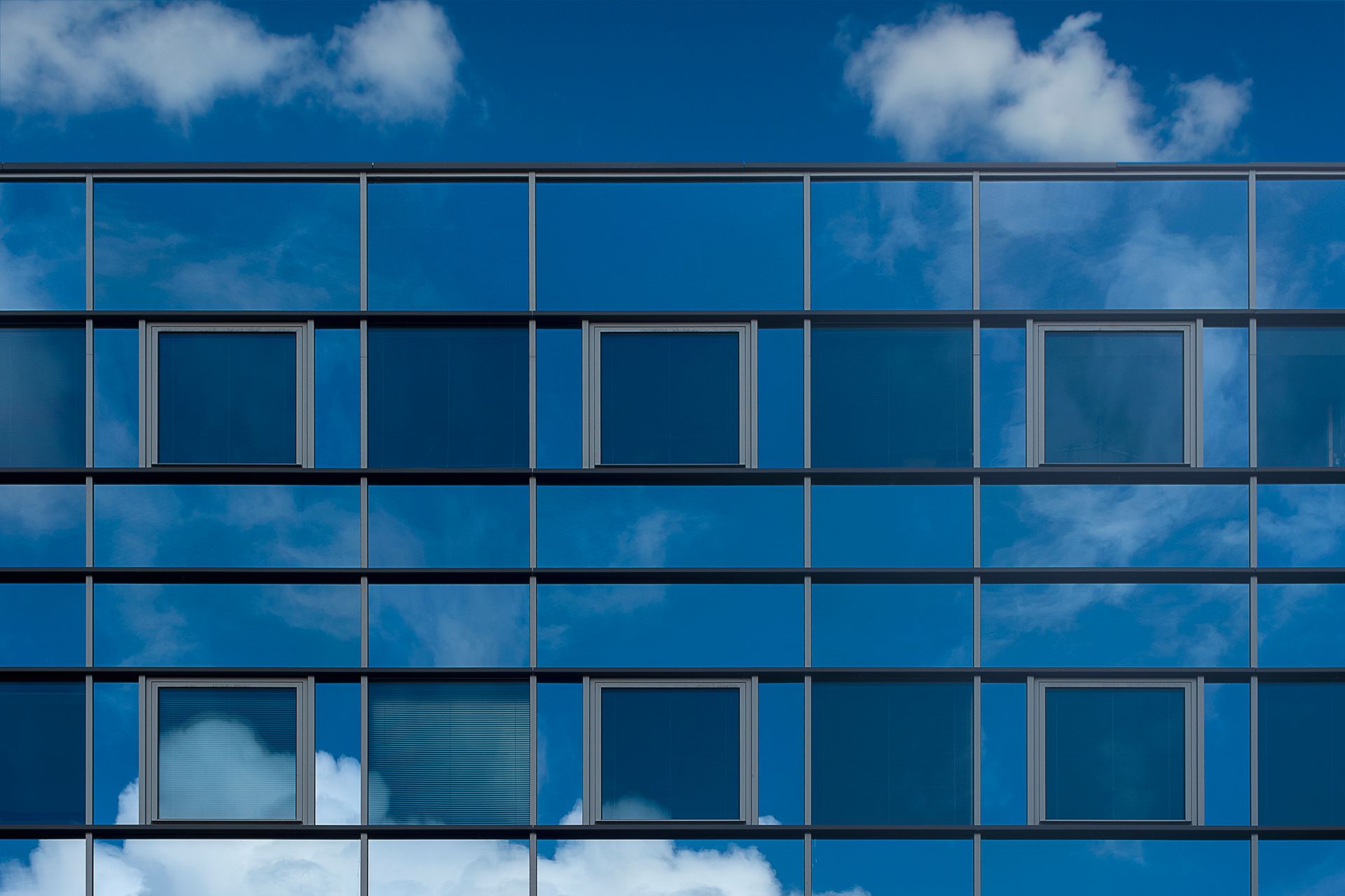 Glass office building facade reflecting a blue sky and clouds