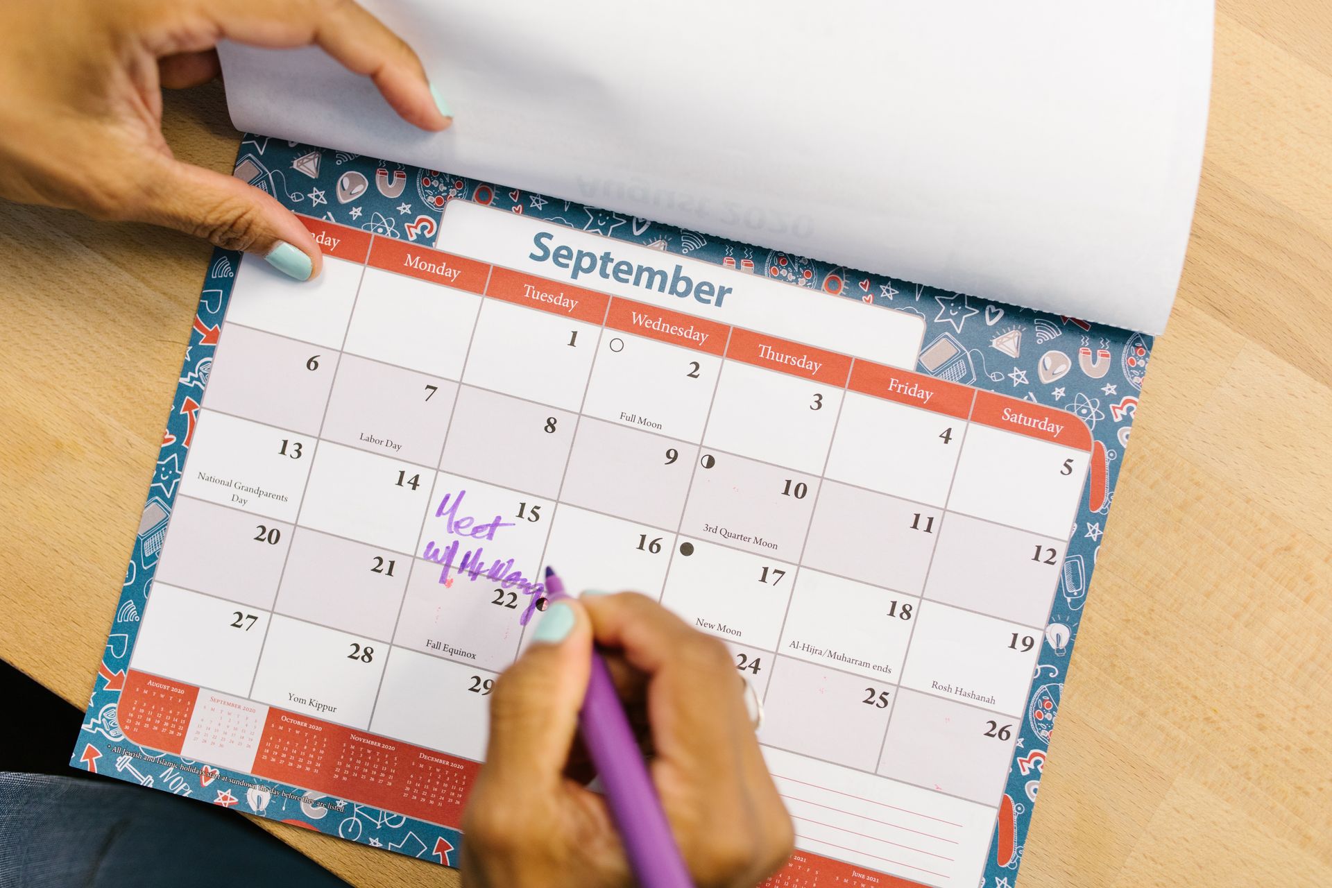 Hands marking dates on a paper calendar on a wooden desk