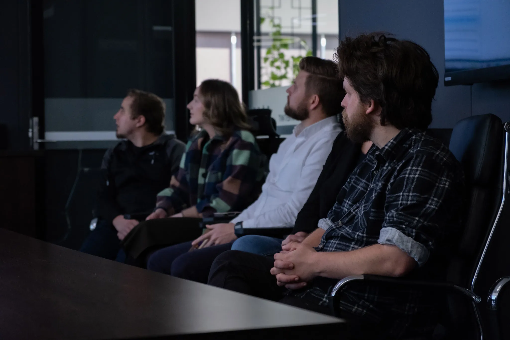 Team members sitting in boardroom around large table looking at presentation screen