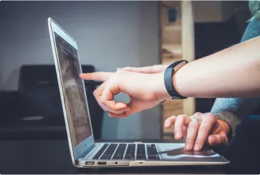 Persons hand pointing at computer screen