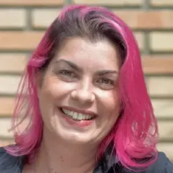 Helena Poças Leitão é Fundadora do Sua Escola Ideal. Mulher branca de cabelos rosas e olhos claros com terno cinza e camisa branca.