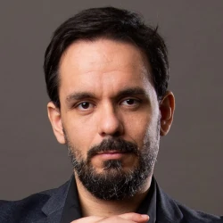 Higor Fabiano é o fundador da Escola de Matrículas. Homem branco de cabelos e olhos pretos, de terno e camisa. 