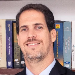 Gustavo Peixoto Nunes. Homem branco de olhos claros, cabelos e barba pretos, de terno azul-marinho, camisa branca e gravata azul.