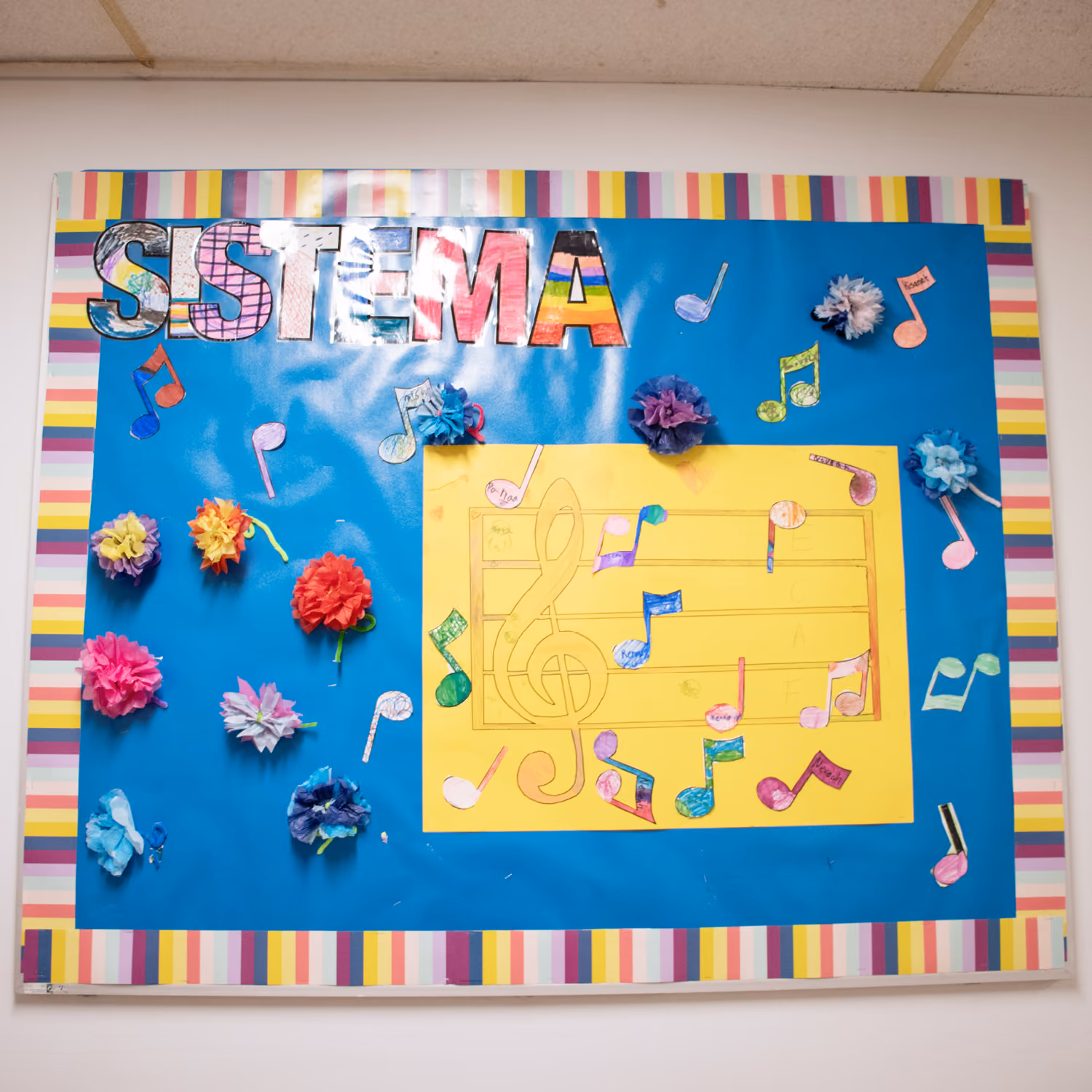 Colorful bulletin board with the word SISTEMA, music notes, and tissue paper flowers on blue background.