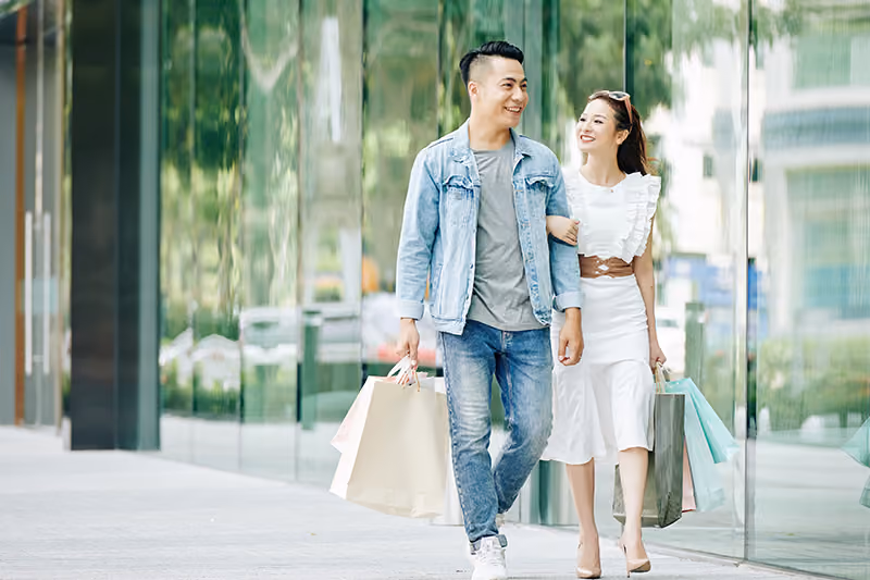 A young couple walks together down a street holding shopping bags