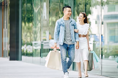 Smiling couple walking with shopping bags near glass building in an urban setting.