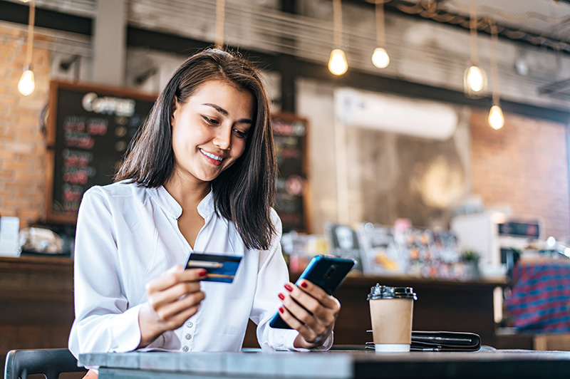Smiling woman holds credit card while at a laptop in a cafe. 