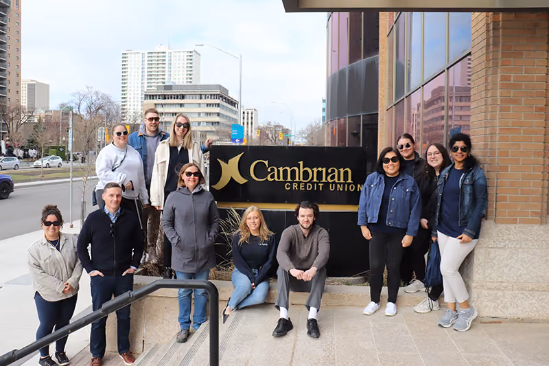 A group of people stand around a Cambrian Credit Union sign
