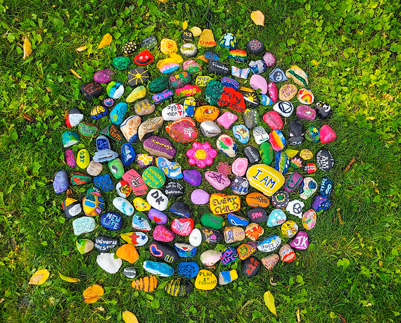 Over 100 colourful painted rocks lying in green grass