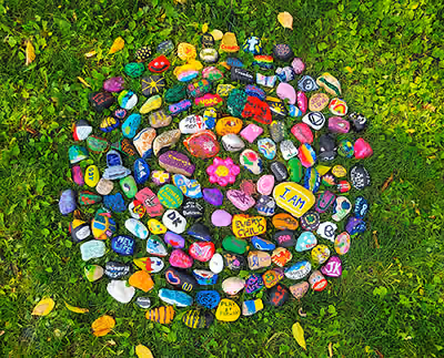 Colorful painted rocks arranged in a circular pattern on green grass outdoors.