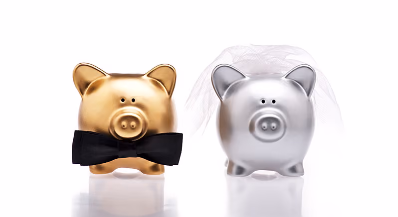 A gold piggy bank with a black bowtie and a silver piggy bank with a veil, side by side