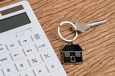 Calculator and house-shaped keychain with a key on a wooden surface.