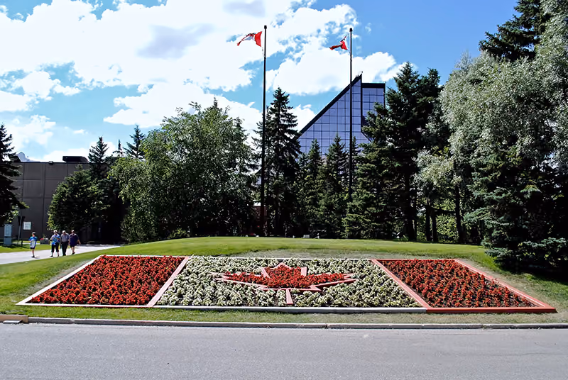 A Canadian flag formed with flowers lies in front of a building surrounded by trees