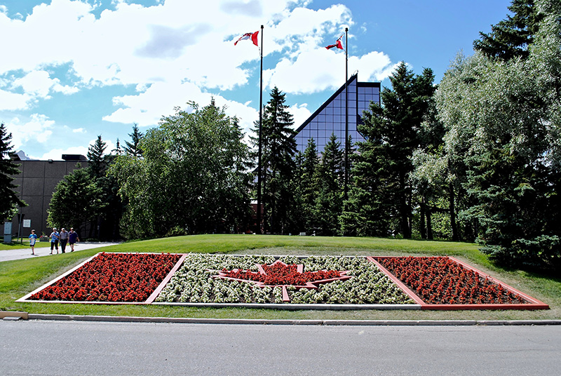 A Canadian flag formed with flowers lies in front of a building surrounded by trees