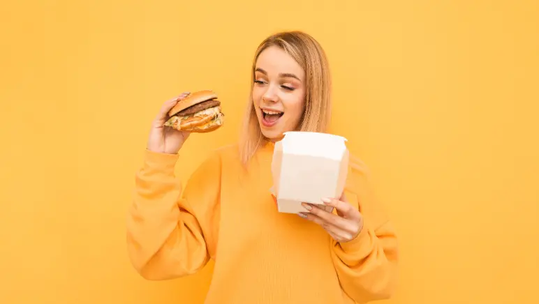 Woman holding a cheeseburger, symbolizing a potential link between poor diet and hernia risk.