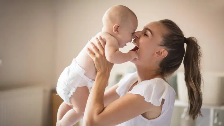 New mom holding her baby while touching her abdomen — postpartum hernia awareness.