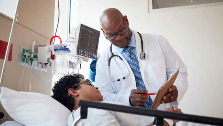 Doctor explaining urgent hernia surgery to a patient who is laying in a hospital bed.