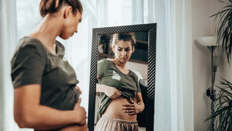 Person holding bloated stomach after hernia surgery recovery.