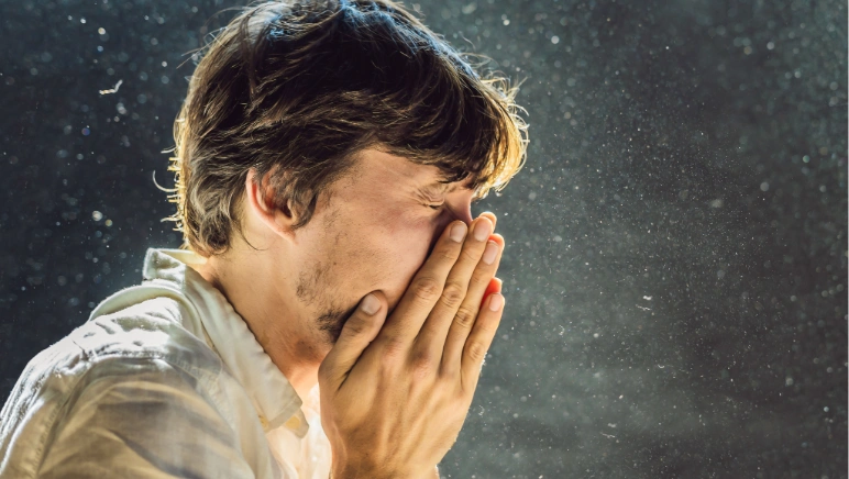 Man trying to stop a sneeze, covering his face with his hands — a sudden sneeze can trigger hernia symptoms