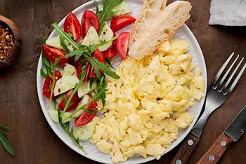 a plate of scrambled eggs, tomatoes, and bread