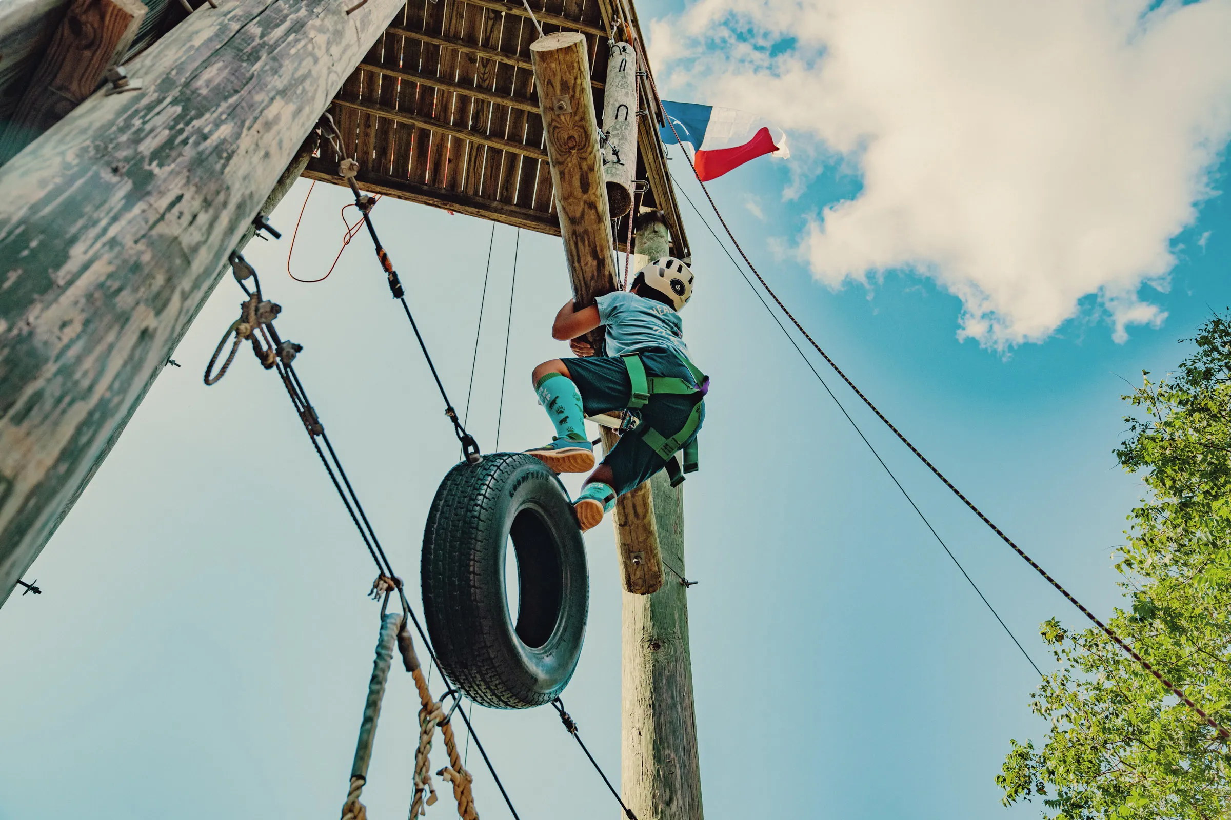 Child climbing a ropes course obstacle with a hanging tire at summer camp