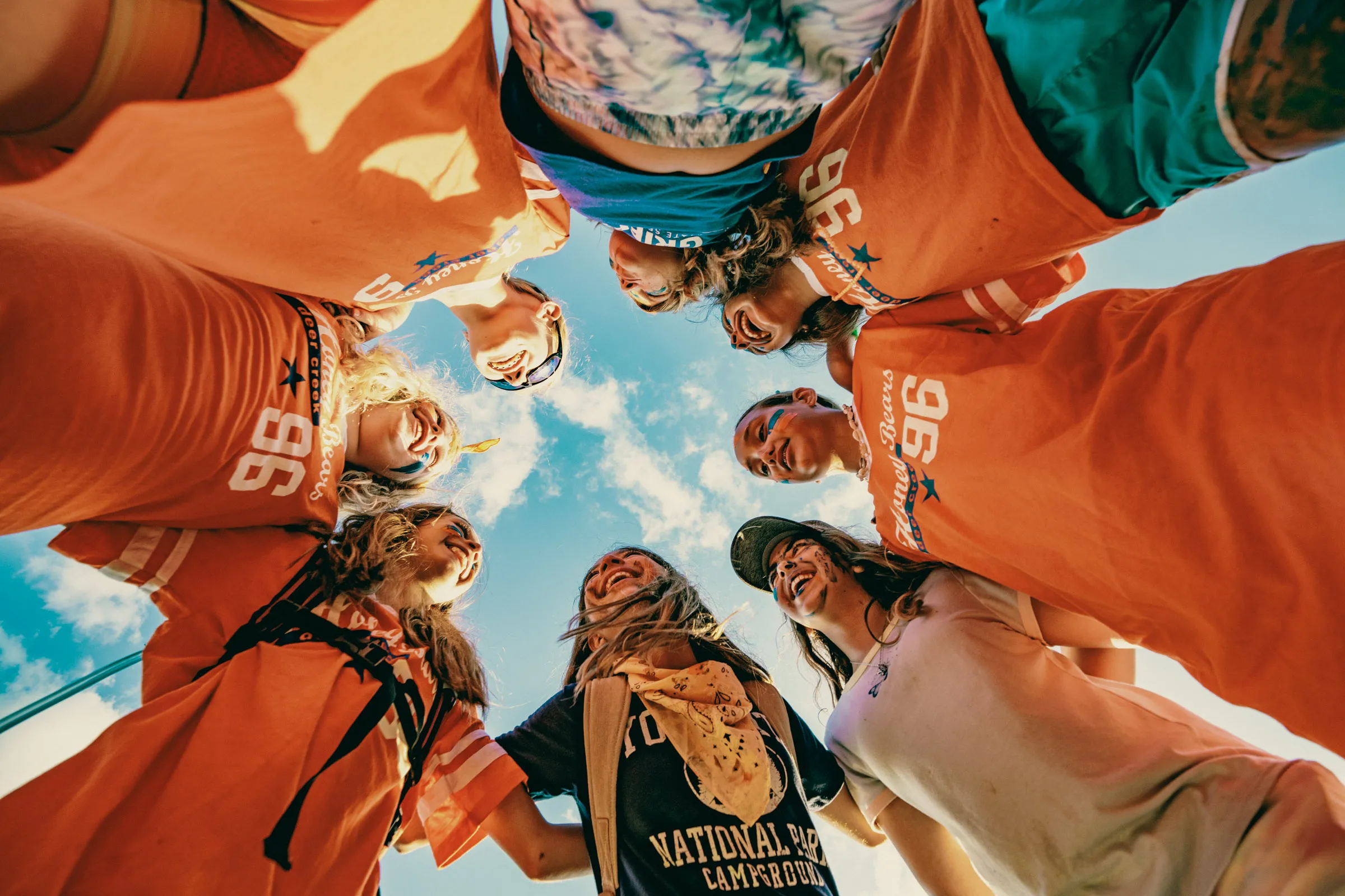 Group of children laughing together in a circle under a blue sky at camp