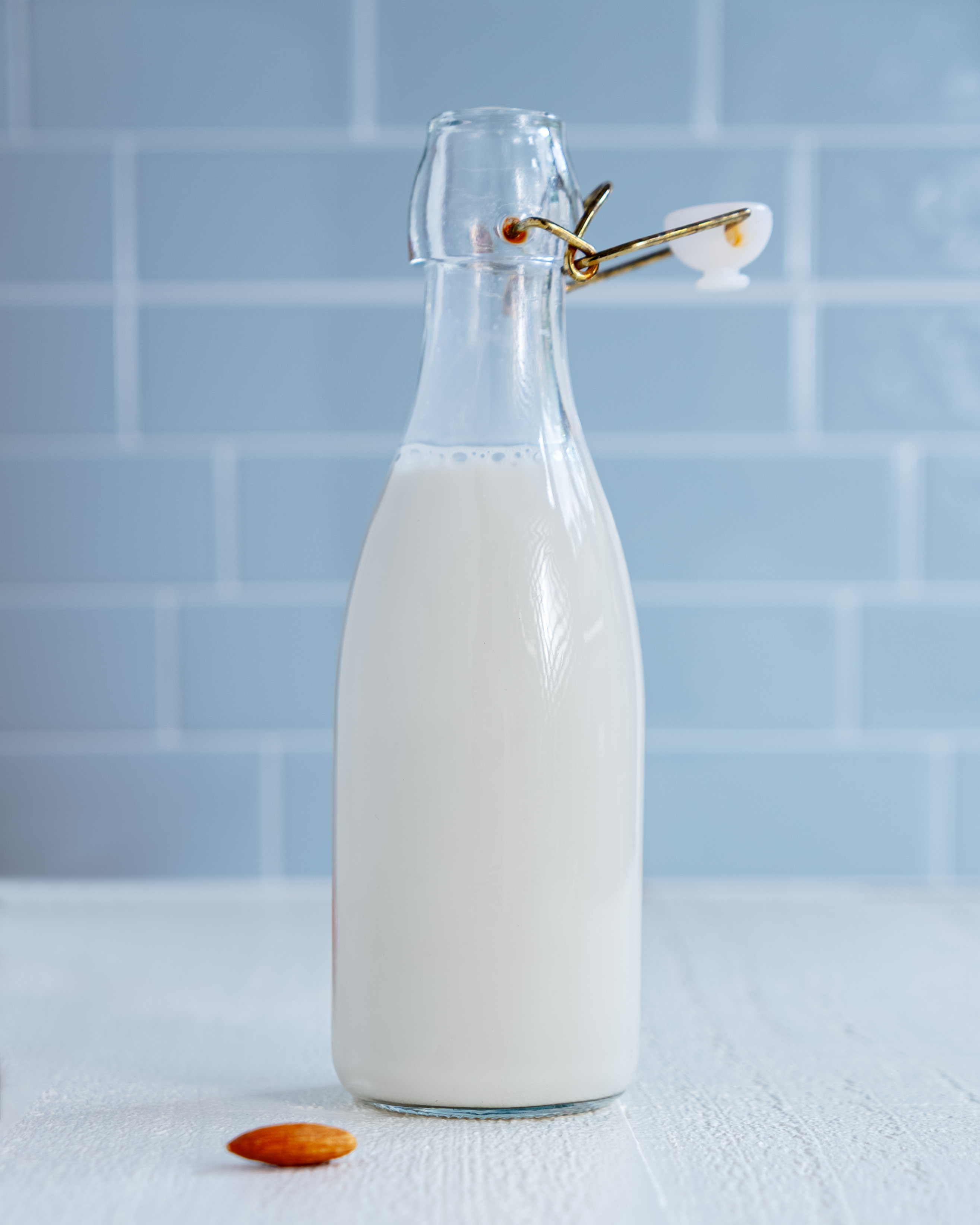Homemade almond milk in a glass bottle with raw almonds scattered on a wooden surface