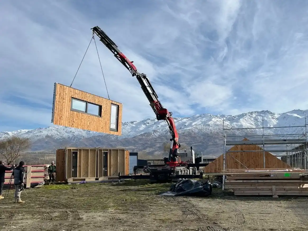 Crane lifting a timber-clad wall panel into position for Flexi House at Electric Cherries, Forest Lodge Orchard.
