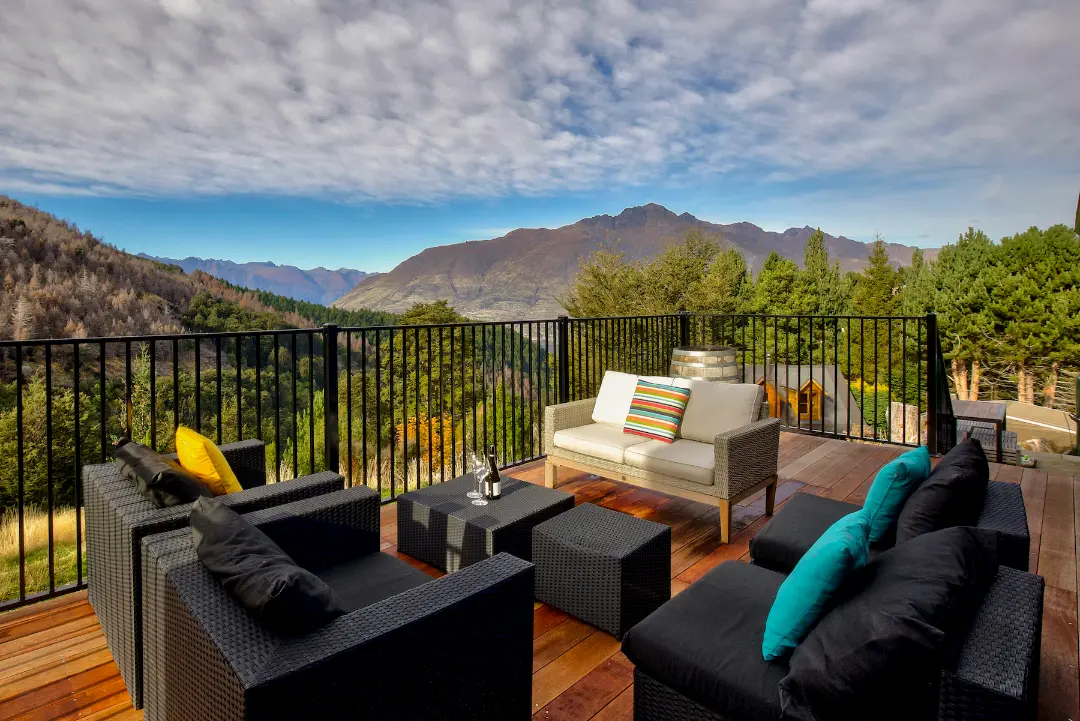 Timber entertaining deck with outdoor sofas and black balustrades framing panoramic mountain views.