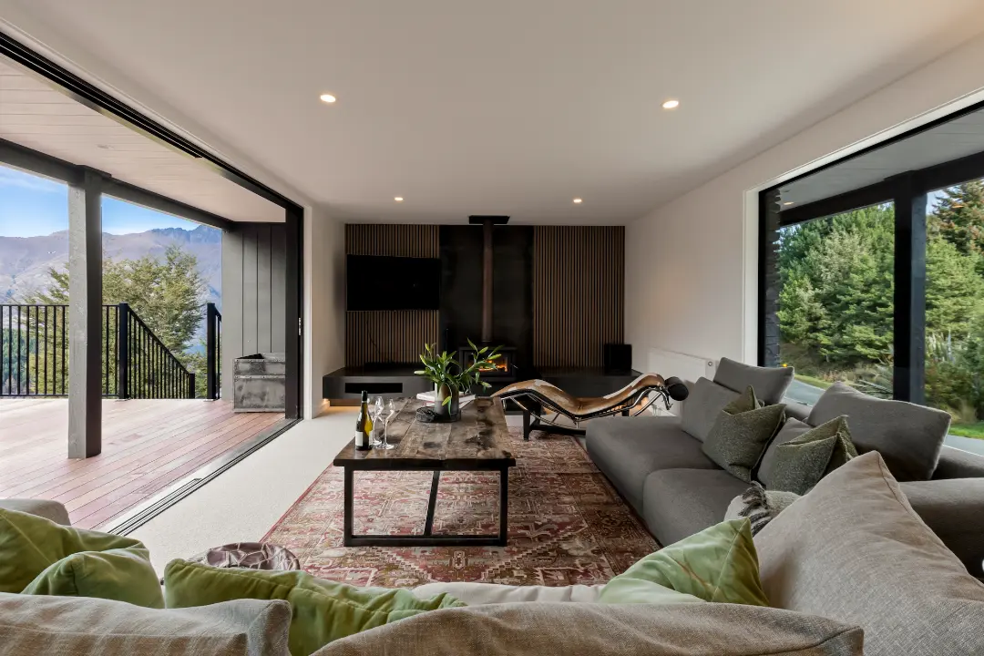 Living room with grey sofas, a wood burner and a wide opening onto the timber deck and mountain views.