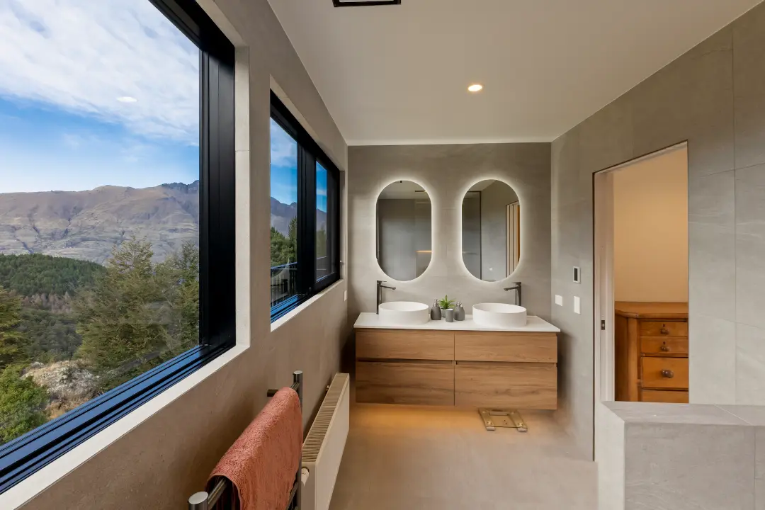 Bathroom with a floating timber double vanity, oval mirrors and large windows framing the mountain landscape.