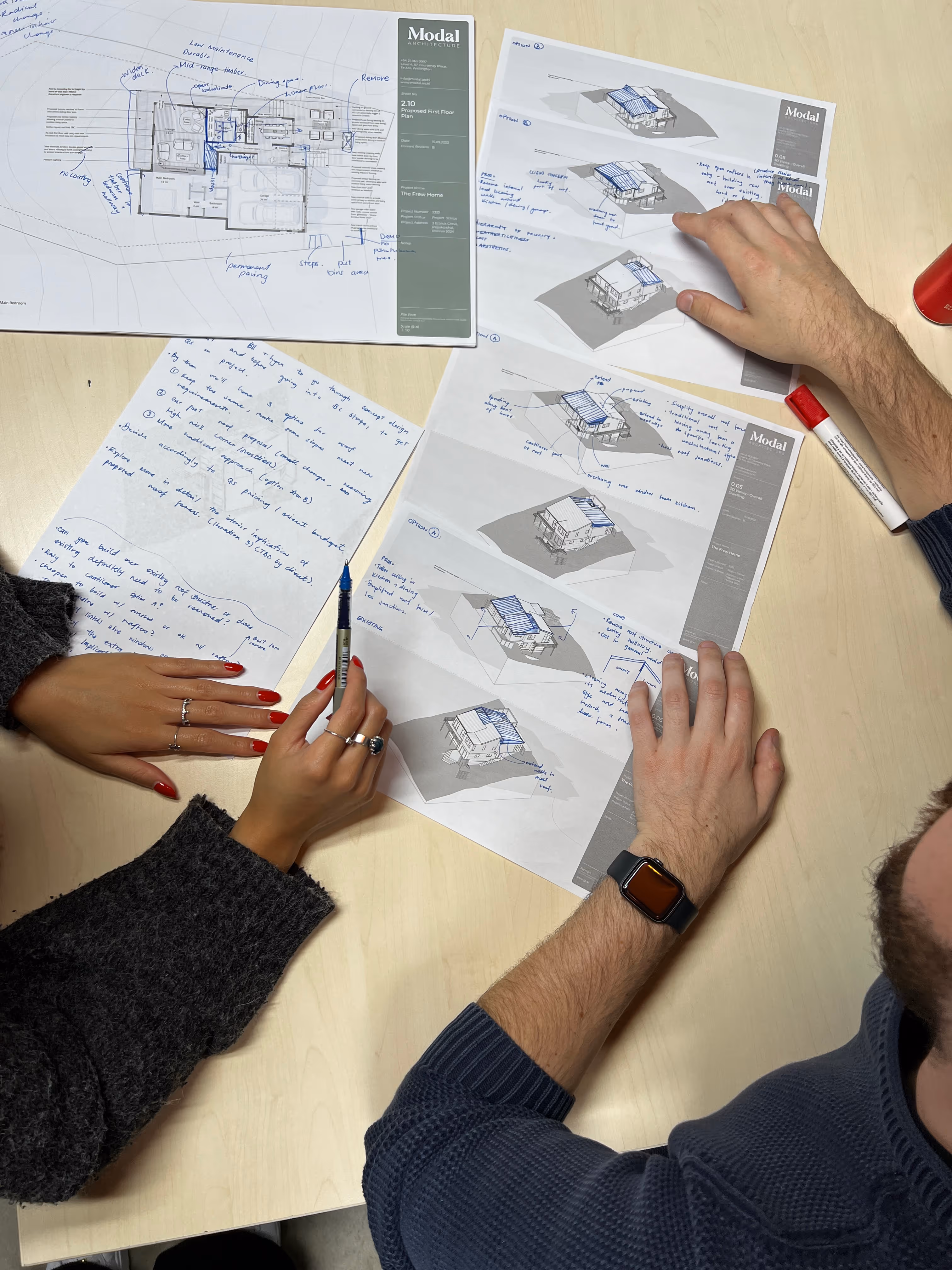 Two people reviewing architectural plans and notes with handwritten annotations on a table. Modal Architecture. New Zealand.