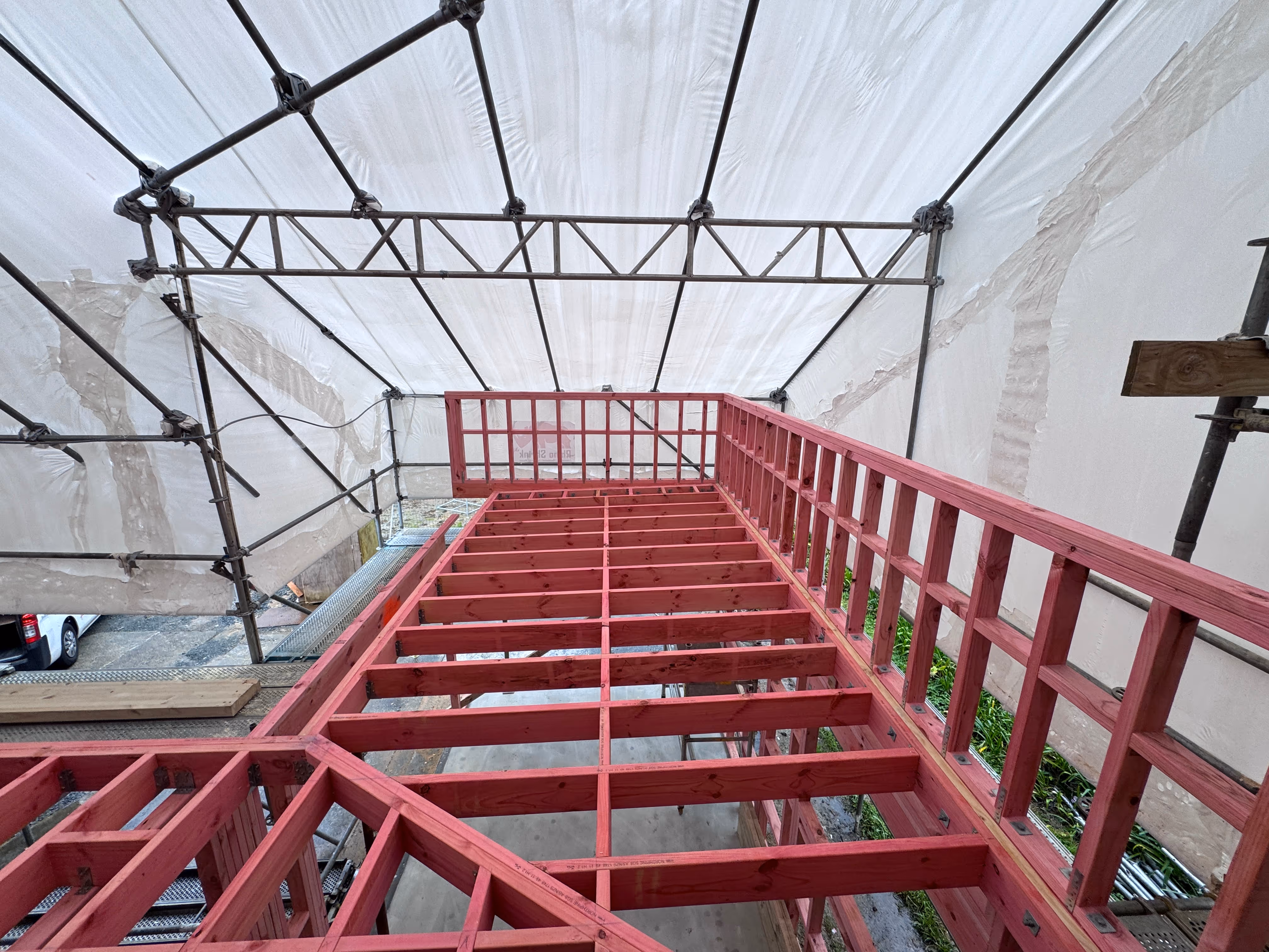 Framing of a timber deck over a membrane roof, under a white protective tent. Modal Architecture. New Zealand.
