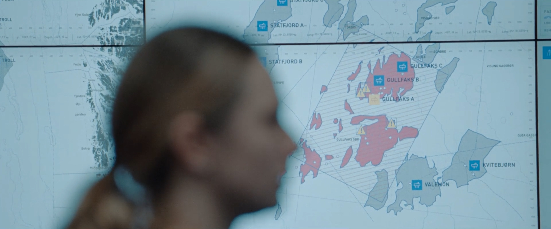 Blurred profile of a person in front of a large map showing offshore oil fields labeled Gullfaks, Statfjord, Valemon, and Kvitebjørn.