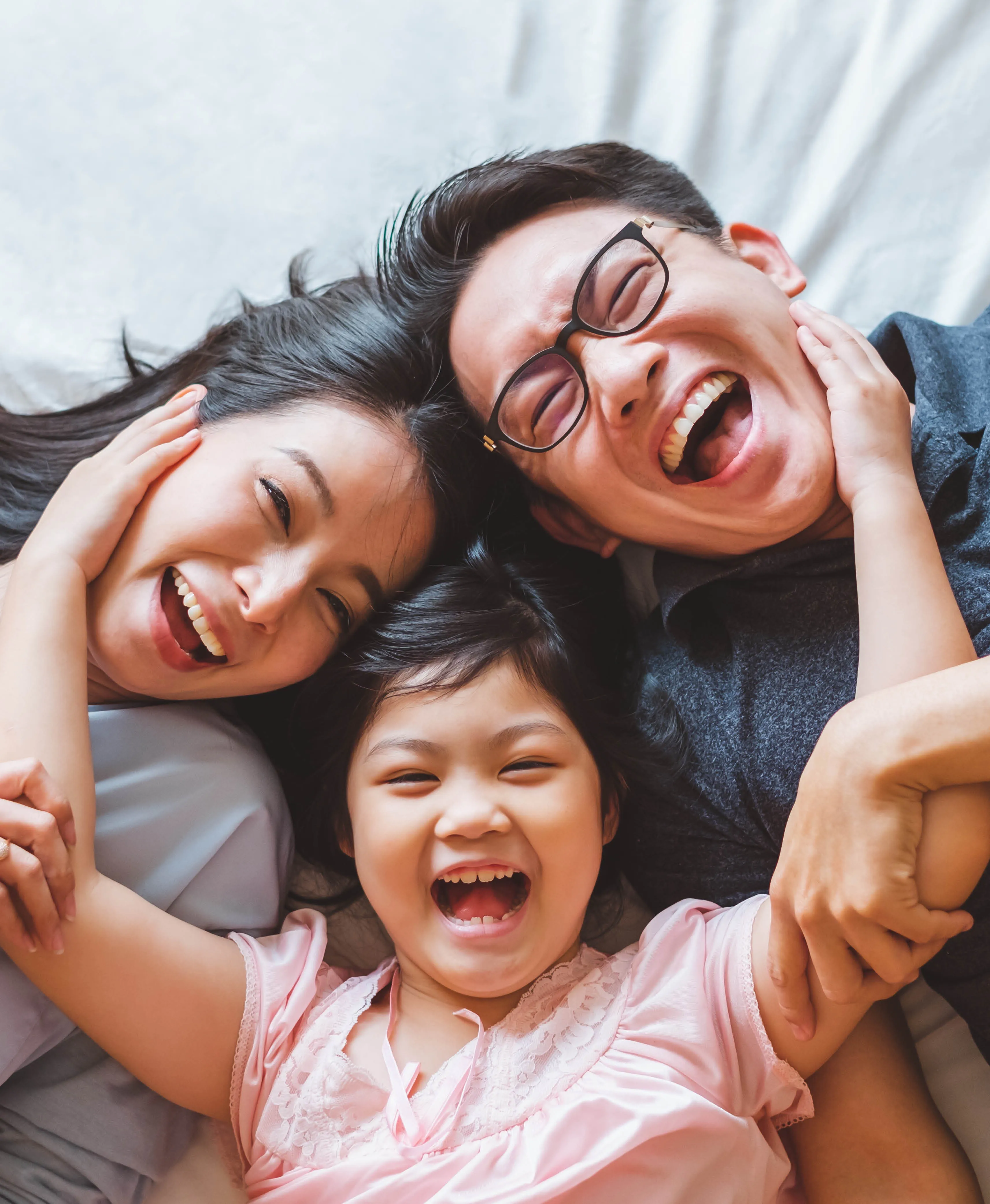 Smiling family of three lying on a bed, with parents and child laughing and holding each other.