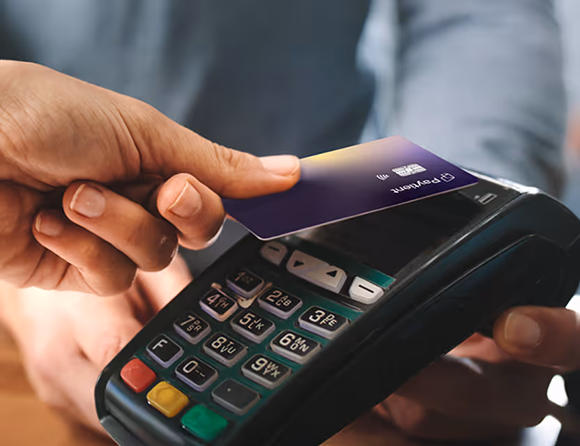 Person holding a Paytient contactless payment card over a card reader terminal for payment transaction.