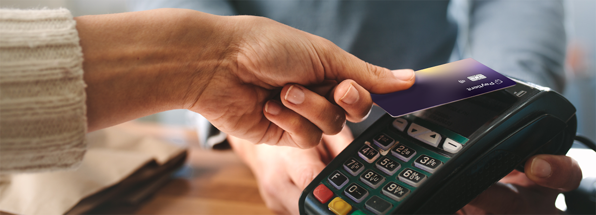 Close-up of a hand holding a purple Paytient card near a payment terminal for contactless payment.